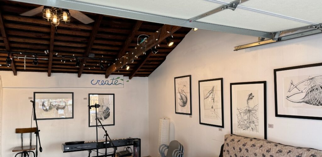 A photo of a garage with gallery lights focused on the framed images hanging on a white walls.